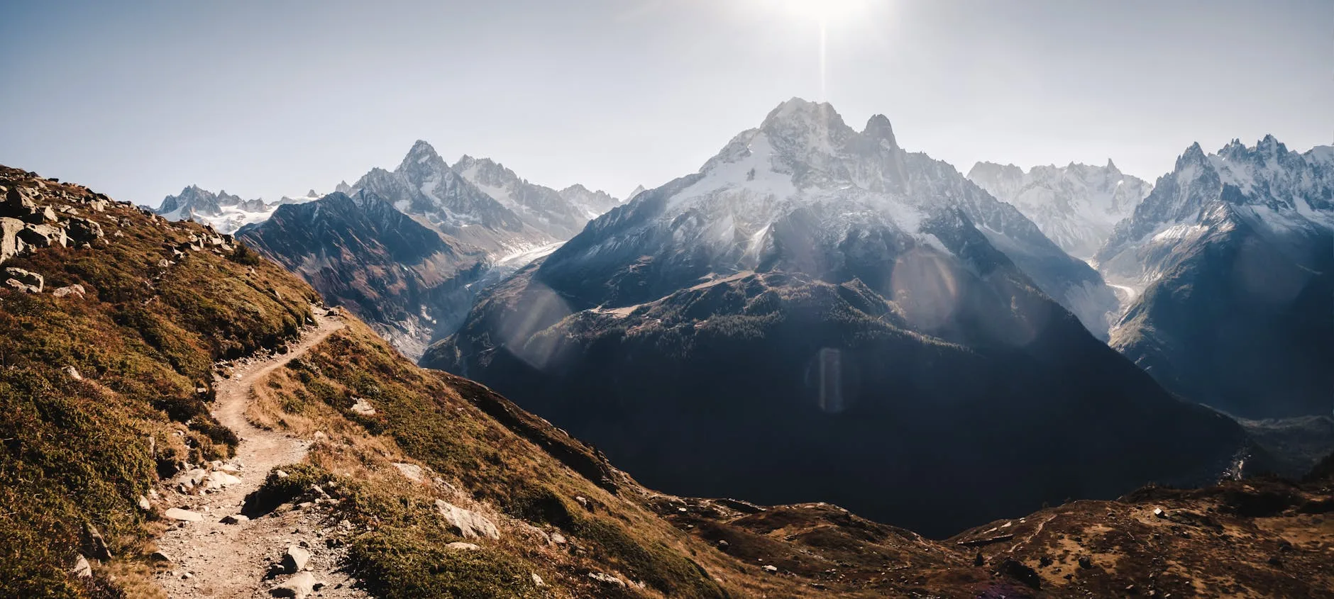 Sunlit rocky trail winding through lush French mountain landscape with distant alpine peaks