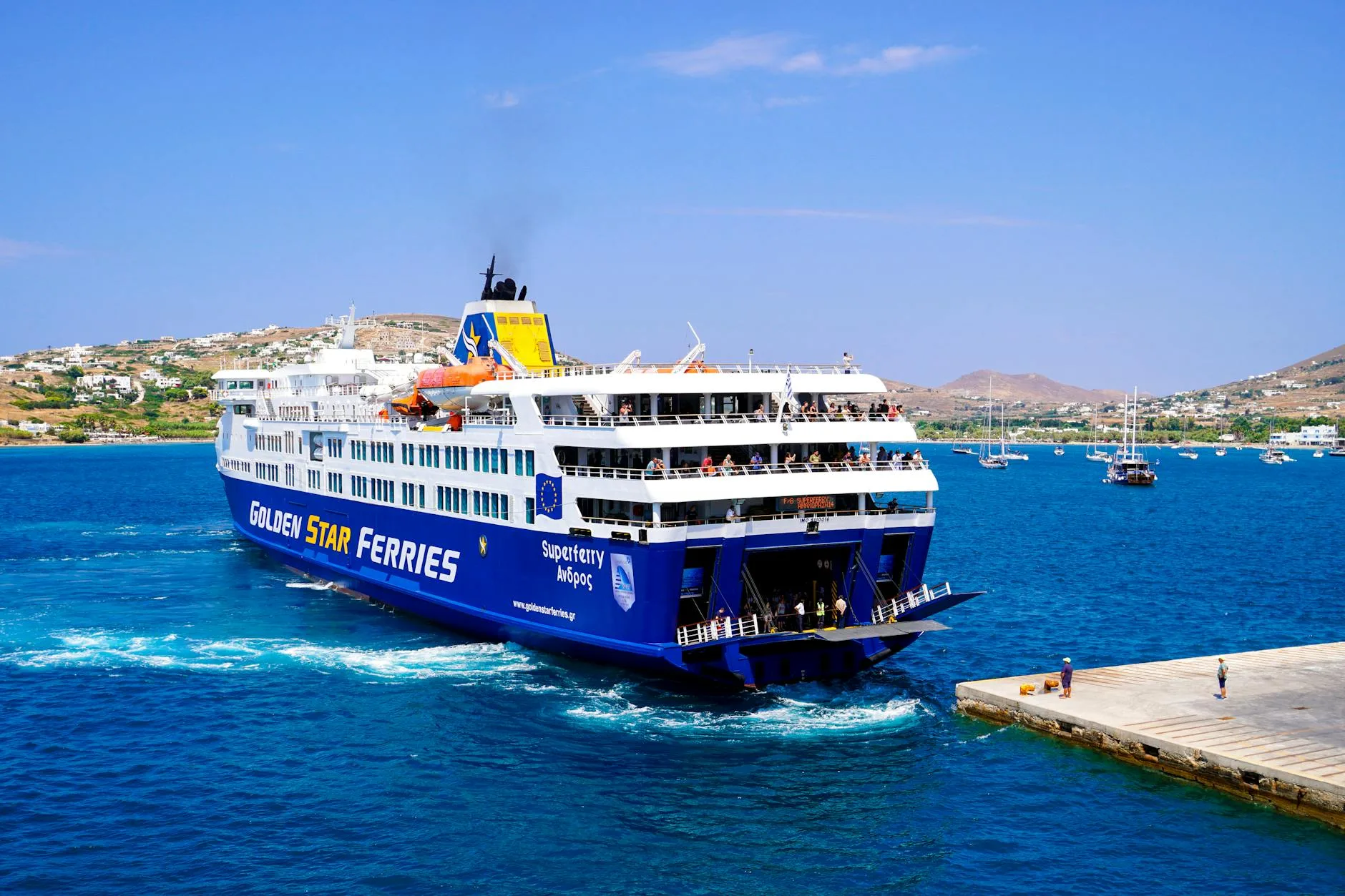 Greek ferry gliding across turquoise Aegean waters toward a sunlit island harbor