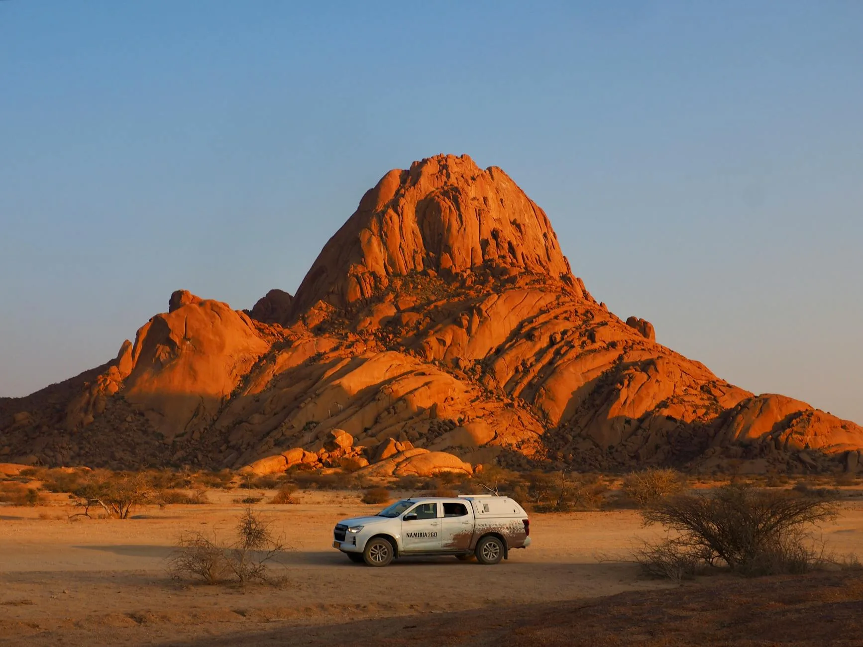 Red gravel road stretching through vast Namibian desert under a blazing orange sunset sky