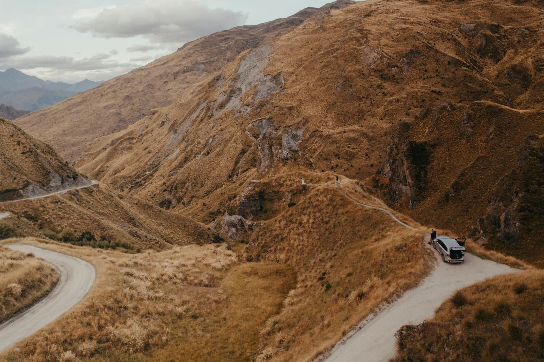 Winding mountain road cutting through lush New Zealand South Island valleys at golden hour