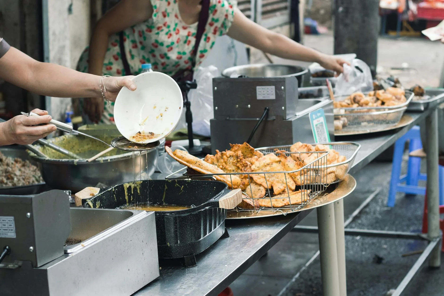 Vendor ladling steaming noodle soup into a bowl at a bustling night market stall