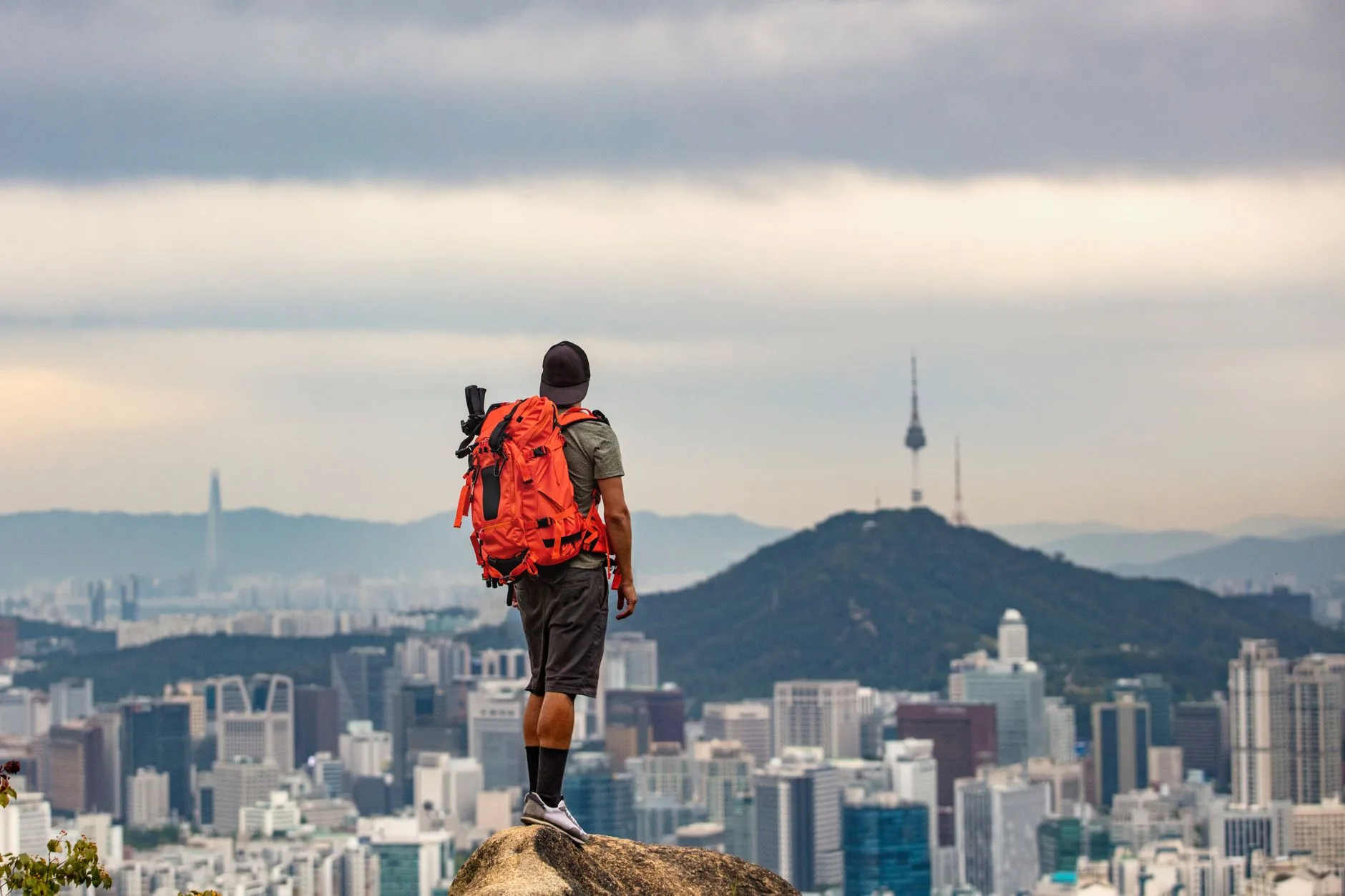 Backpacker hiking misty mountain trail with traditional Korean temple below