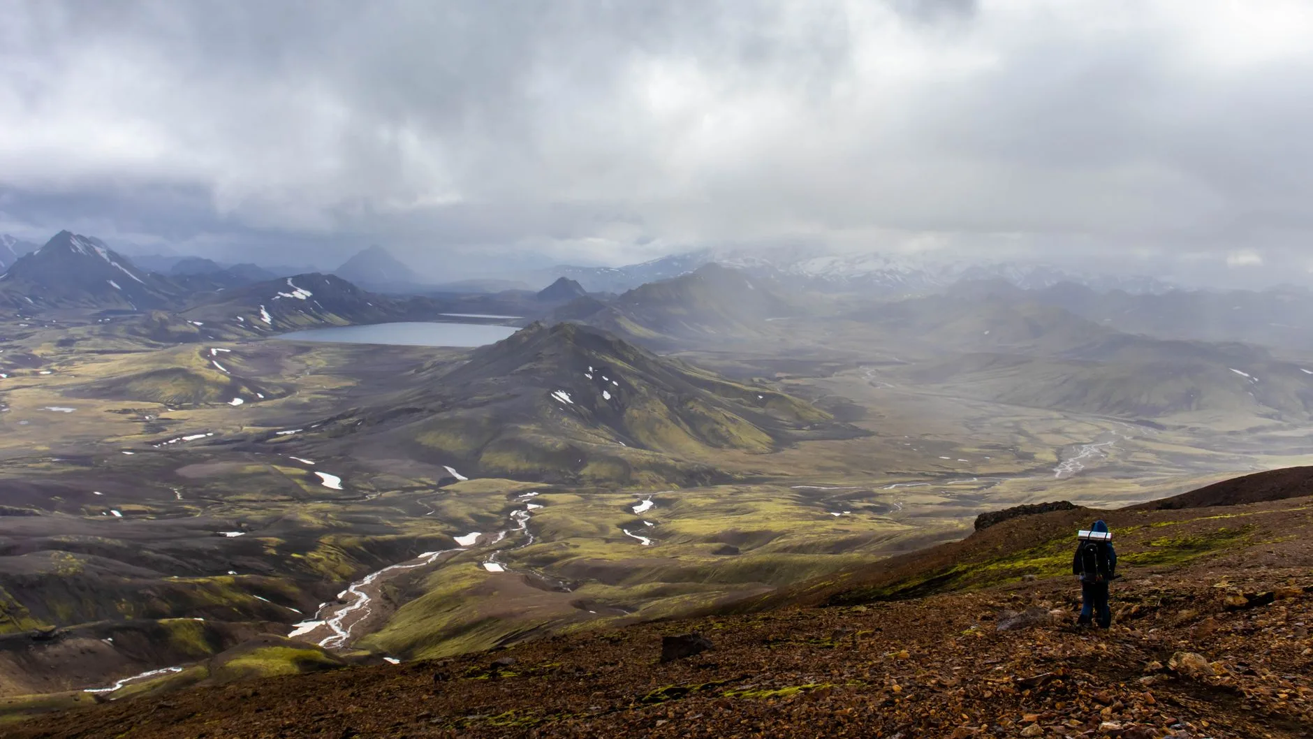 Lone hiker crossing Iceland's vast volcanic landscape under dramatic stormy skies