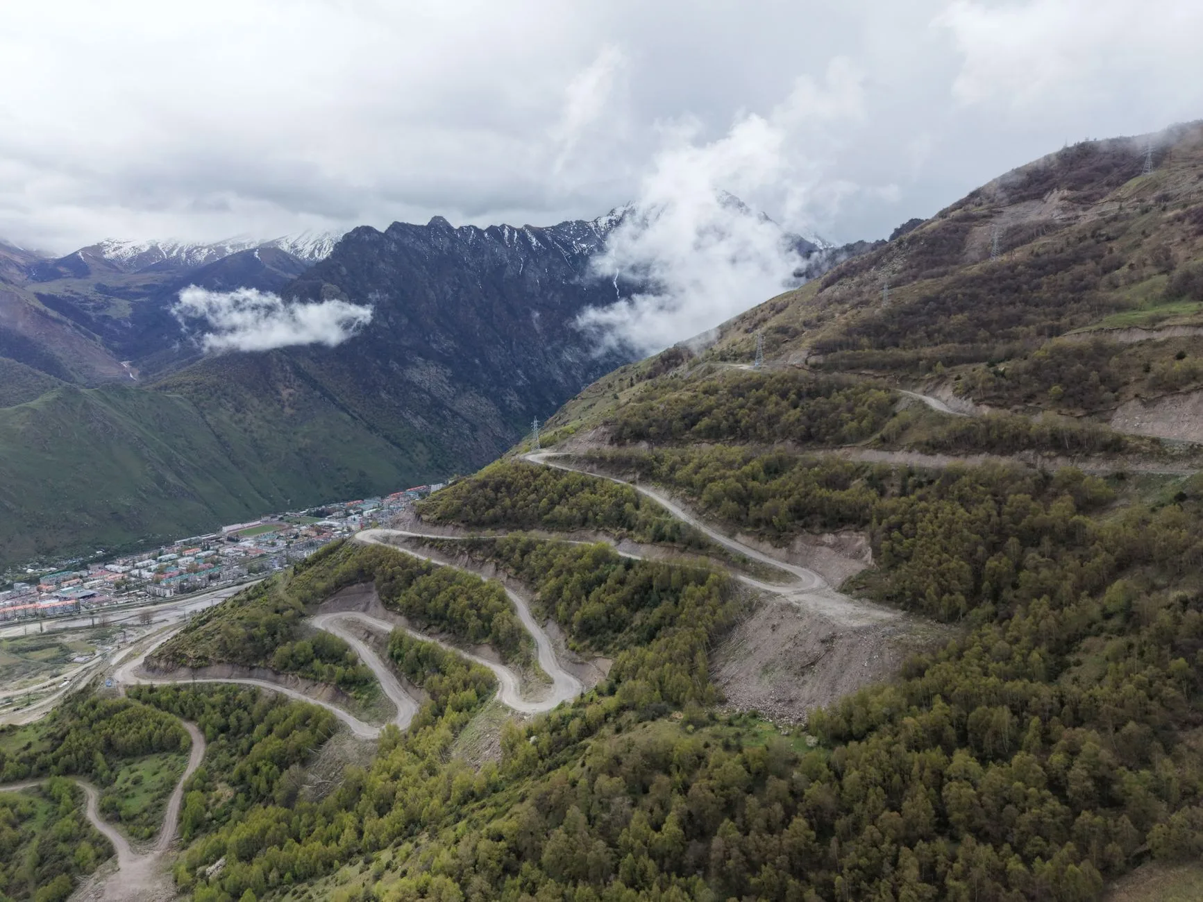 Rugged Caucasus mountain peaks rising above lush green valleys under dramatic skies