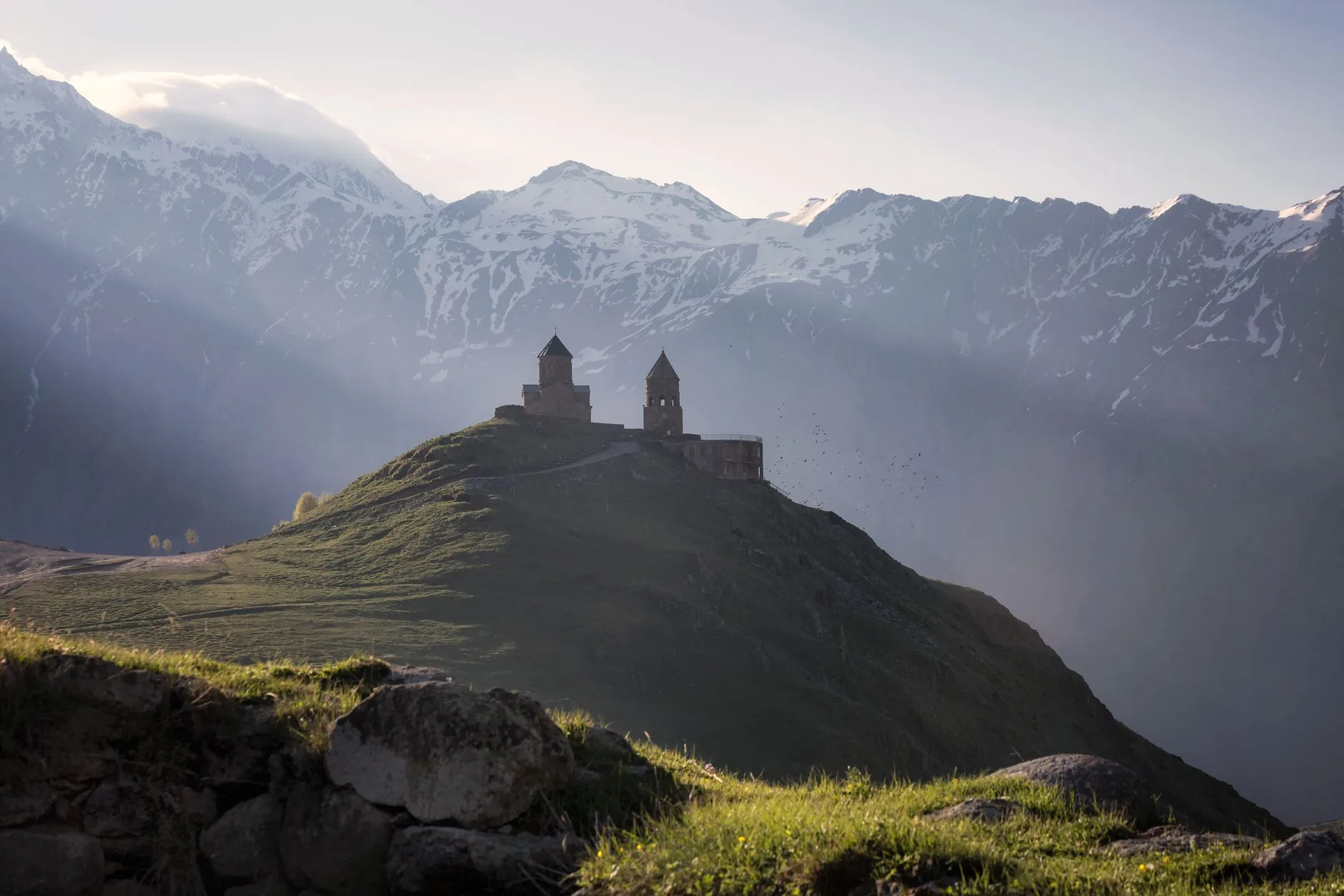 Sunlit ancient Georgian church tower rising above misty Caucasus mountain valleys