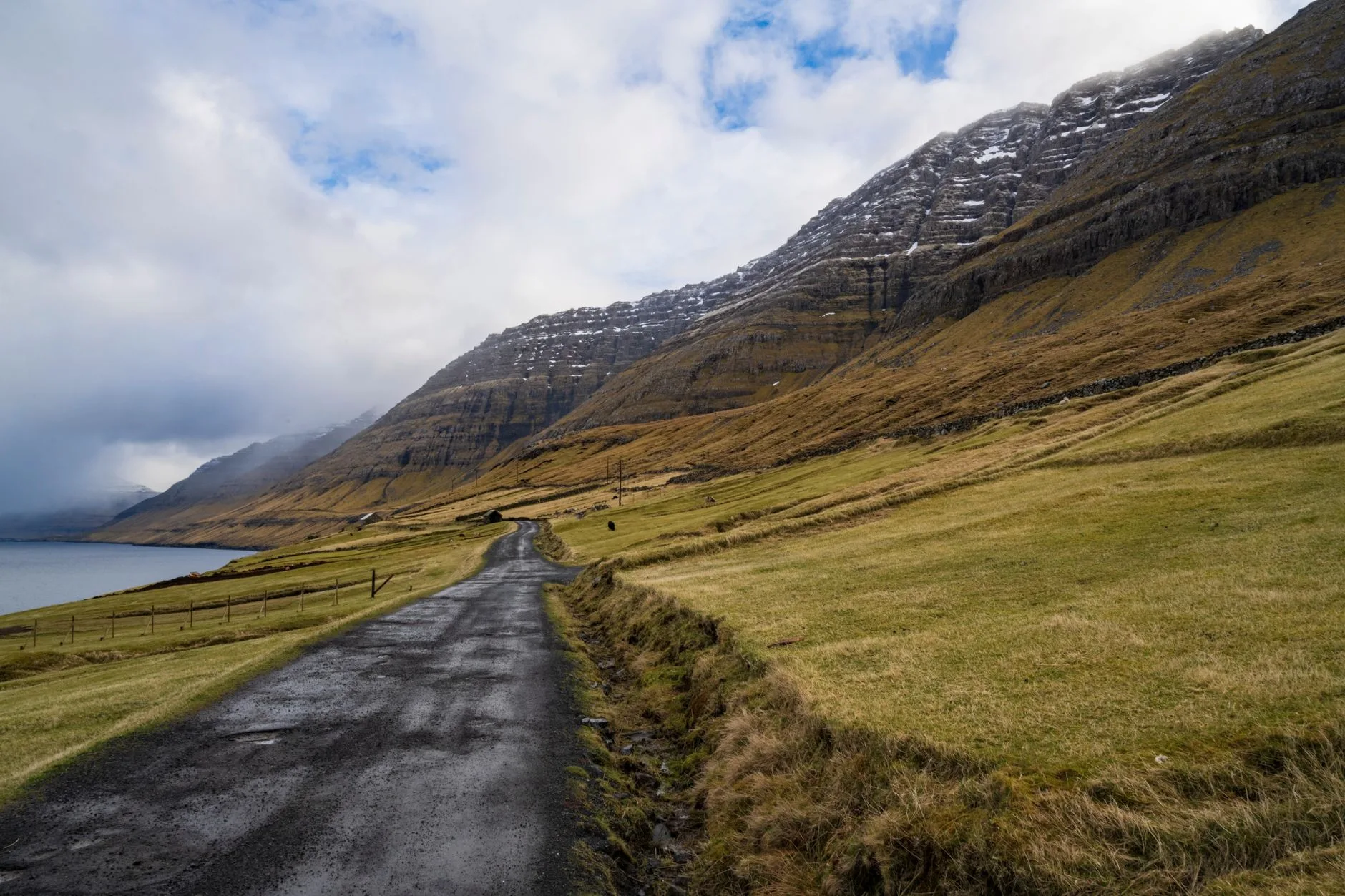 Winding coastal road hugging dramatic Faroese cliffs above churning Atlantic waters