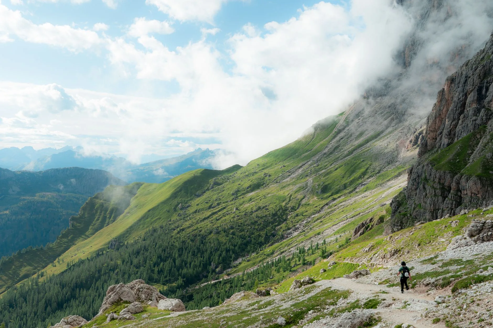 Jagged Dolomite peaks rise above a green alpine valley along a winding hiking trail