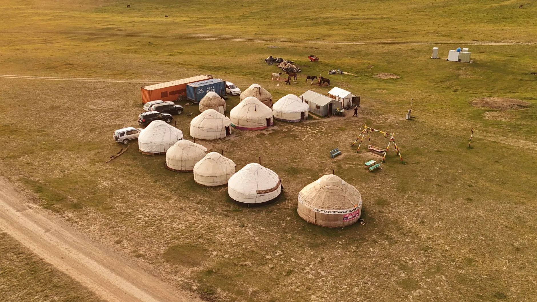 Rider on horseback leading pack horses across a grassy valley near traditional yurts, Kyrgyzstan