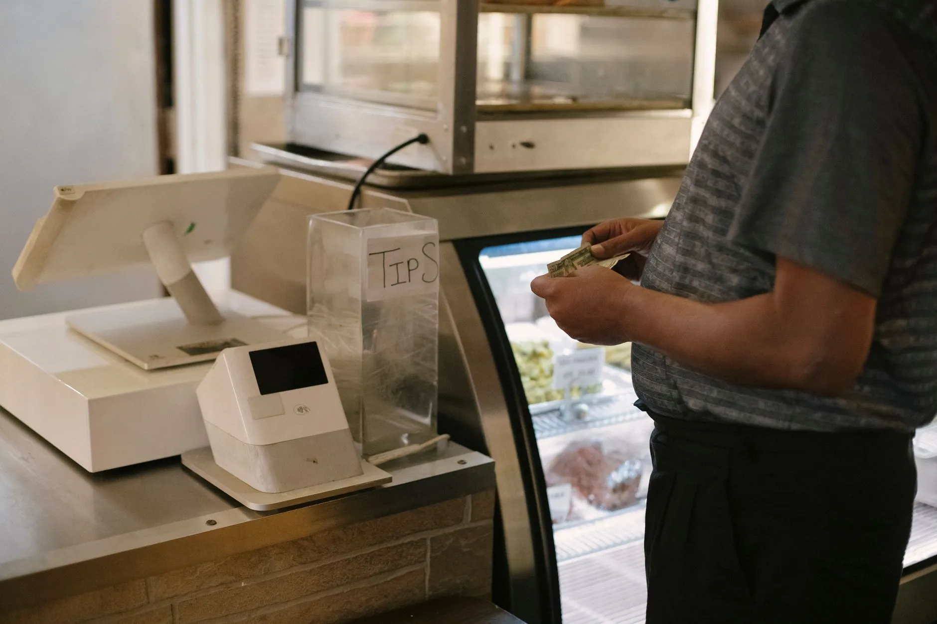 Hand placing cash on a restaurant bill tray beside coins and a coffee cup