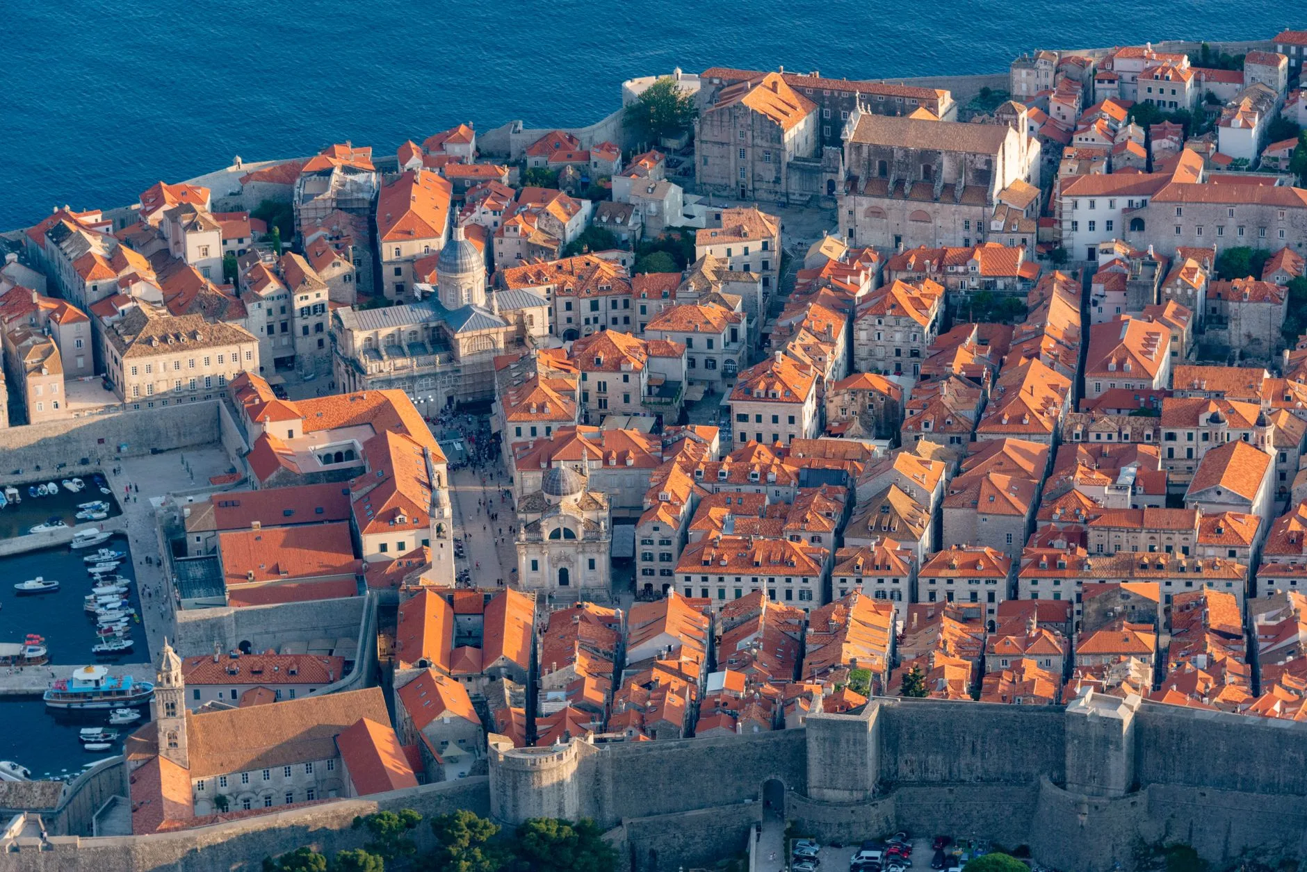 Coastal Croatian town with red-roofed stone houses along a calm turquoise bay at dusk