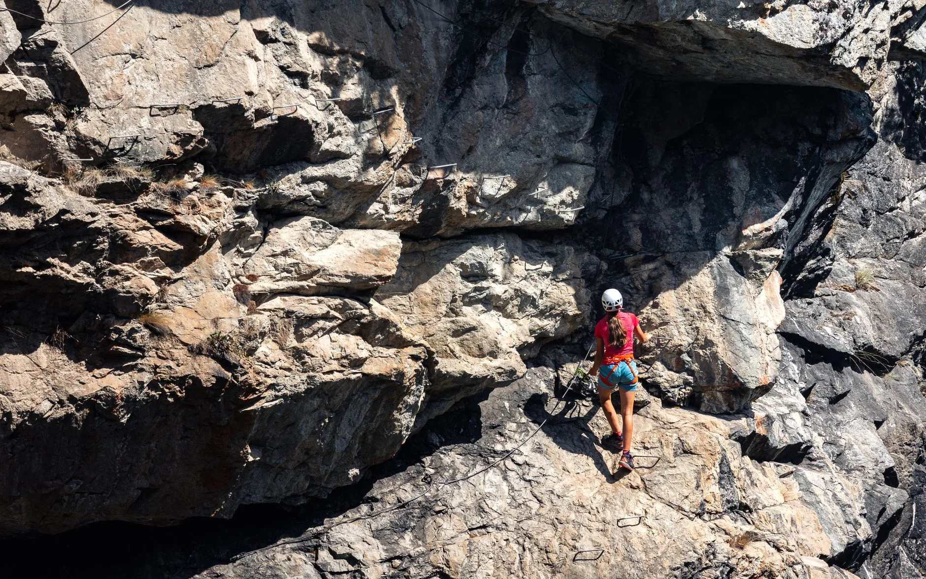 Climber clipped to cable on a via ferrata route, scaling rocky cliffs in the Alps