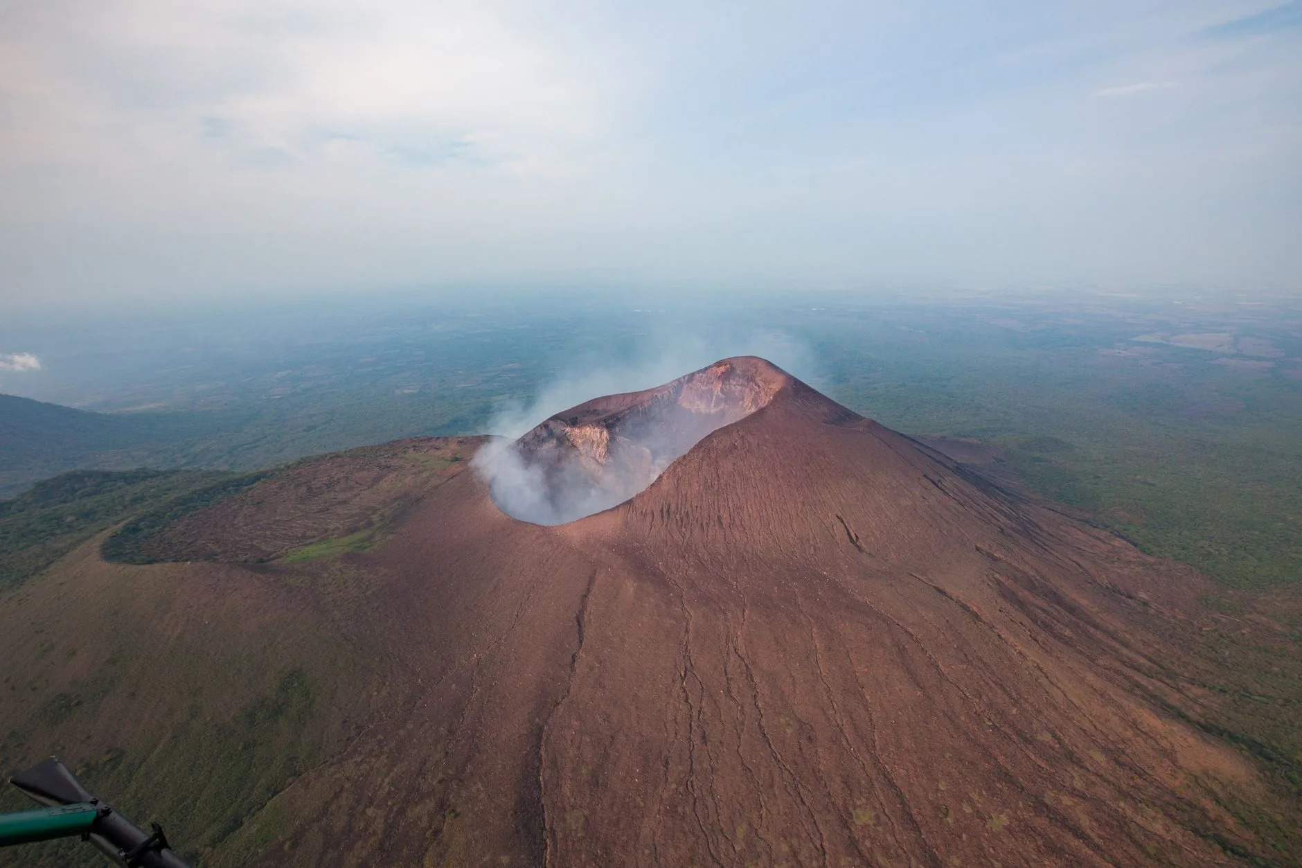 Person sliding down Cerro Negro's black volcanic slope on a wooden board, dust trailing behind