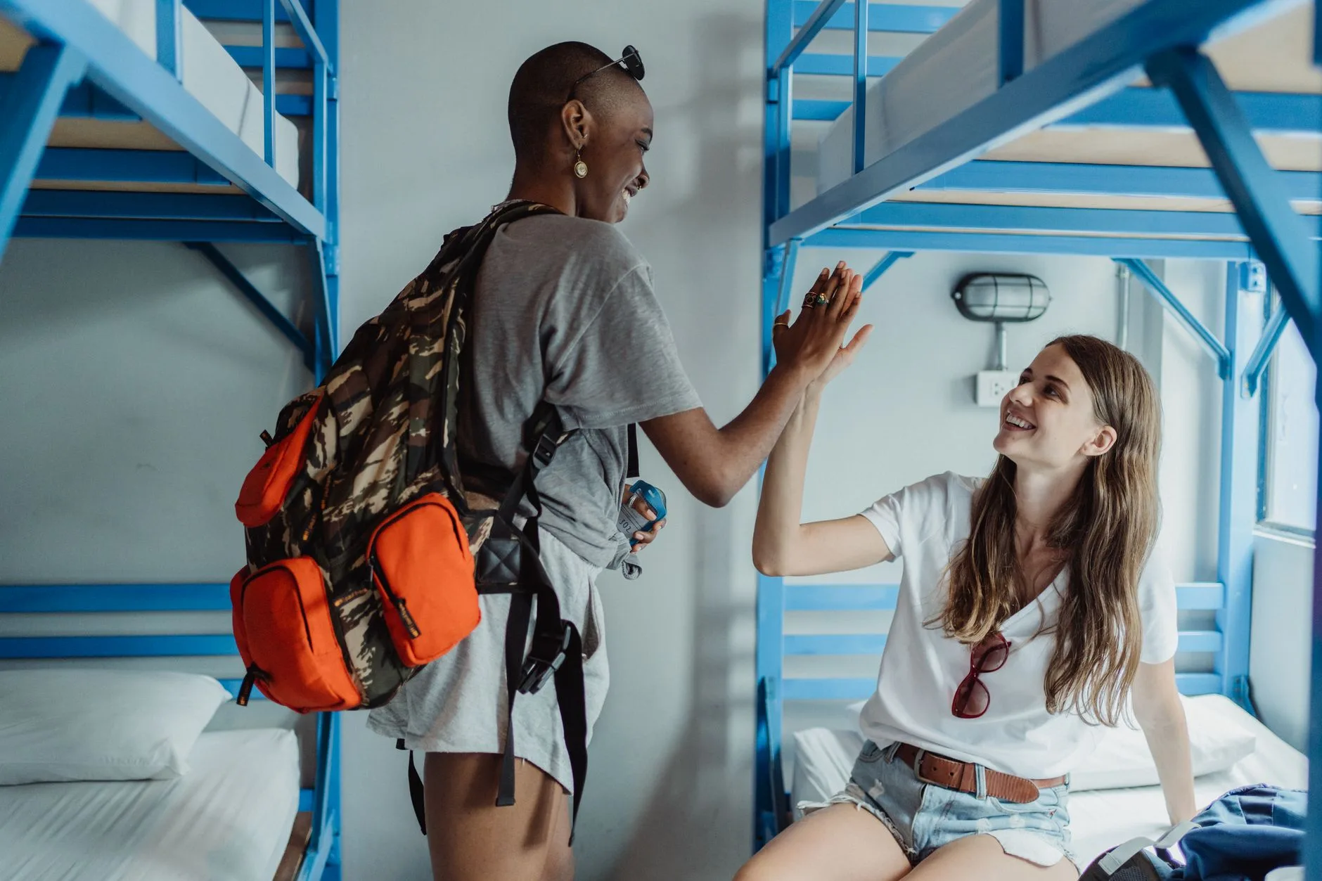 Adult traveler organizing backpack in a sunlit hostel dorm room