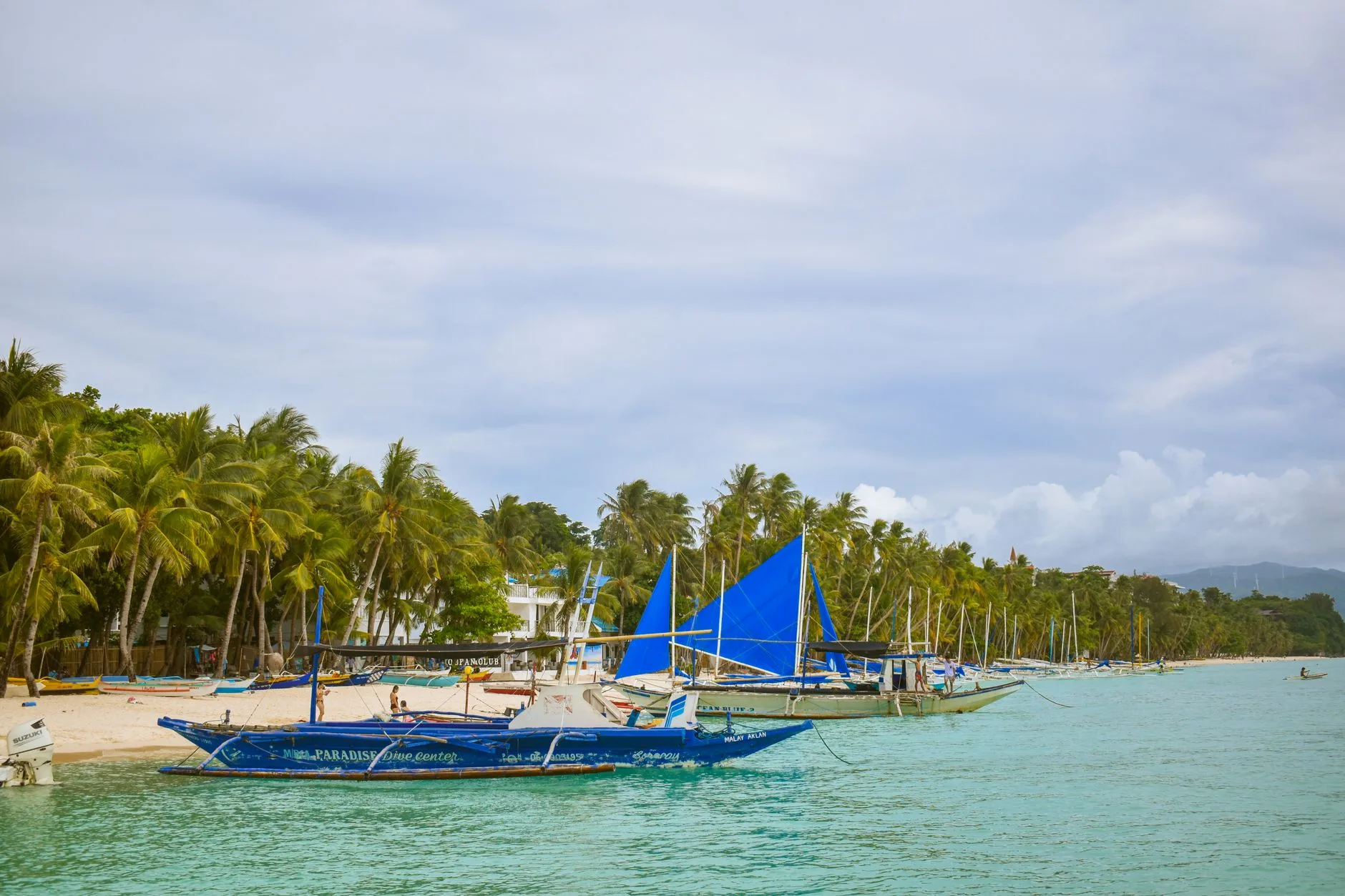 Turquoise bay with wooden boats, limestone cliffs, and palm trees under a clear sky