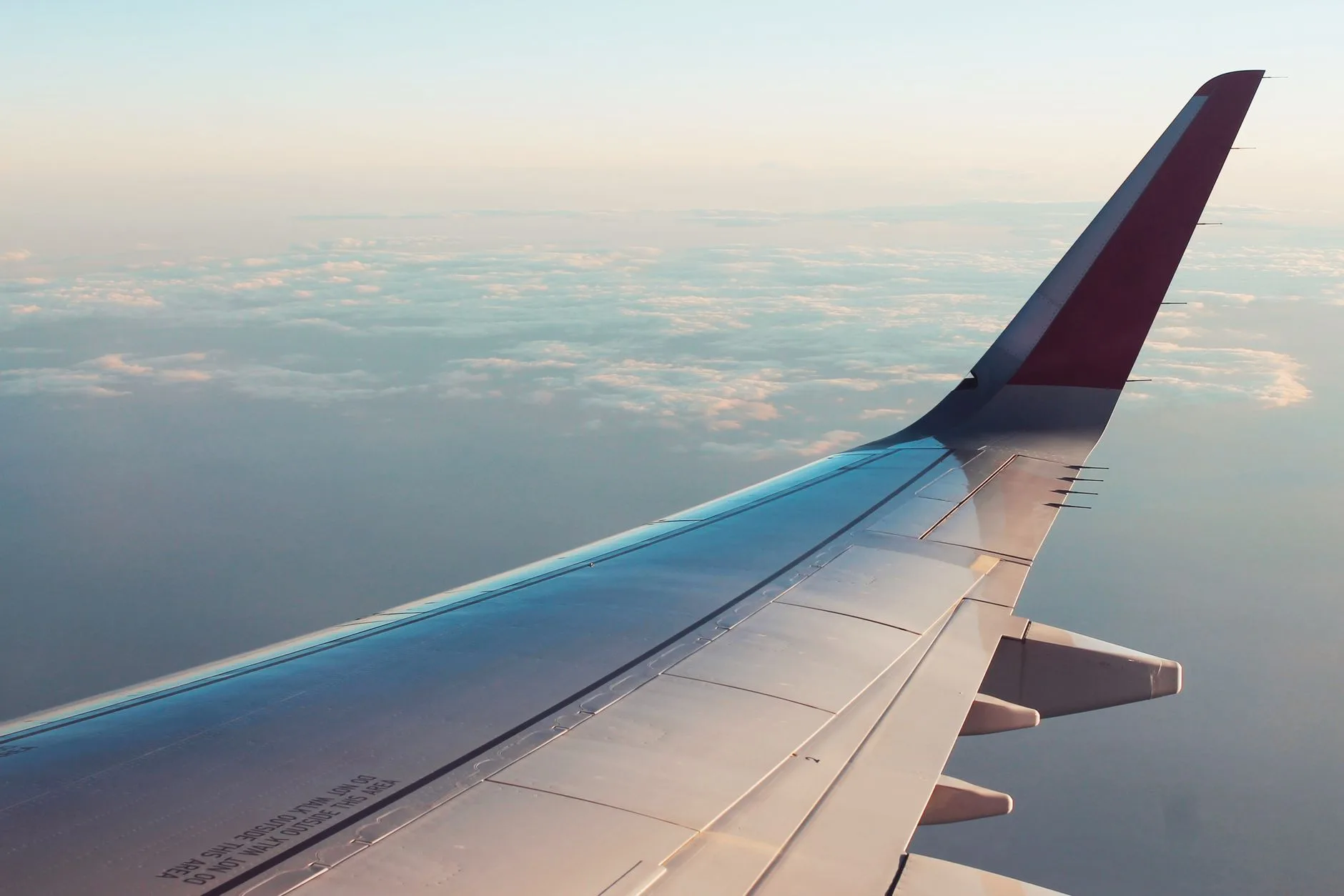 Airplane wing view above clouds at sunset, symbolizing budget travel and flight deals