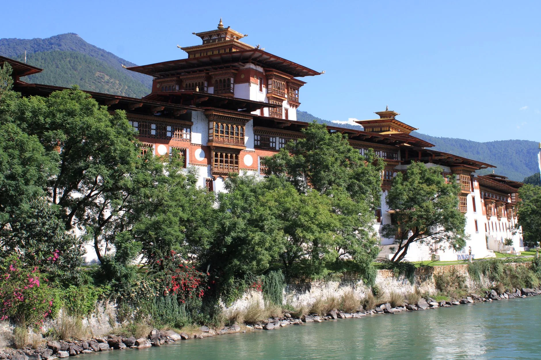 Prayer flags fluttering above a terraced Bhutanese valley, with a monastery on a distant ridge