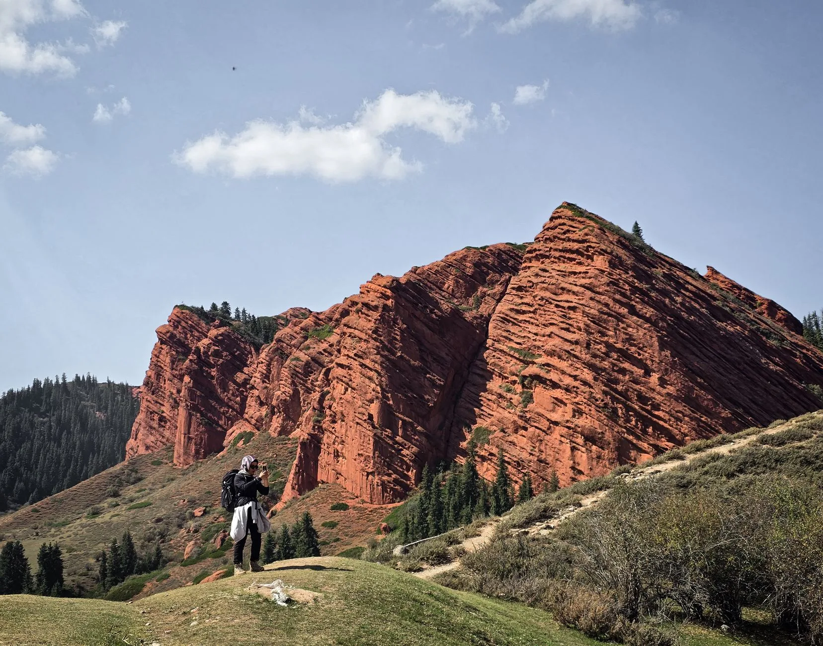 Rolling green hills of Kyrgyzstan with a solitary yurt beneath a vast, cloud-streaked sky.