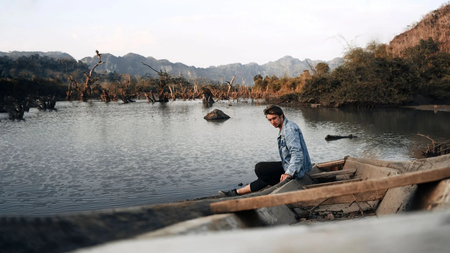 Wooden slow boat drifting down the Mekong River past misty green Laotian hills