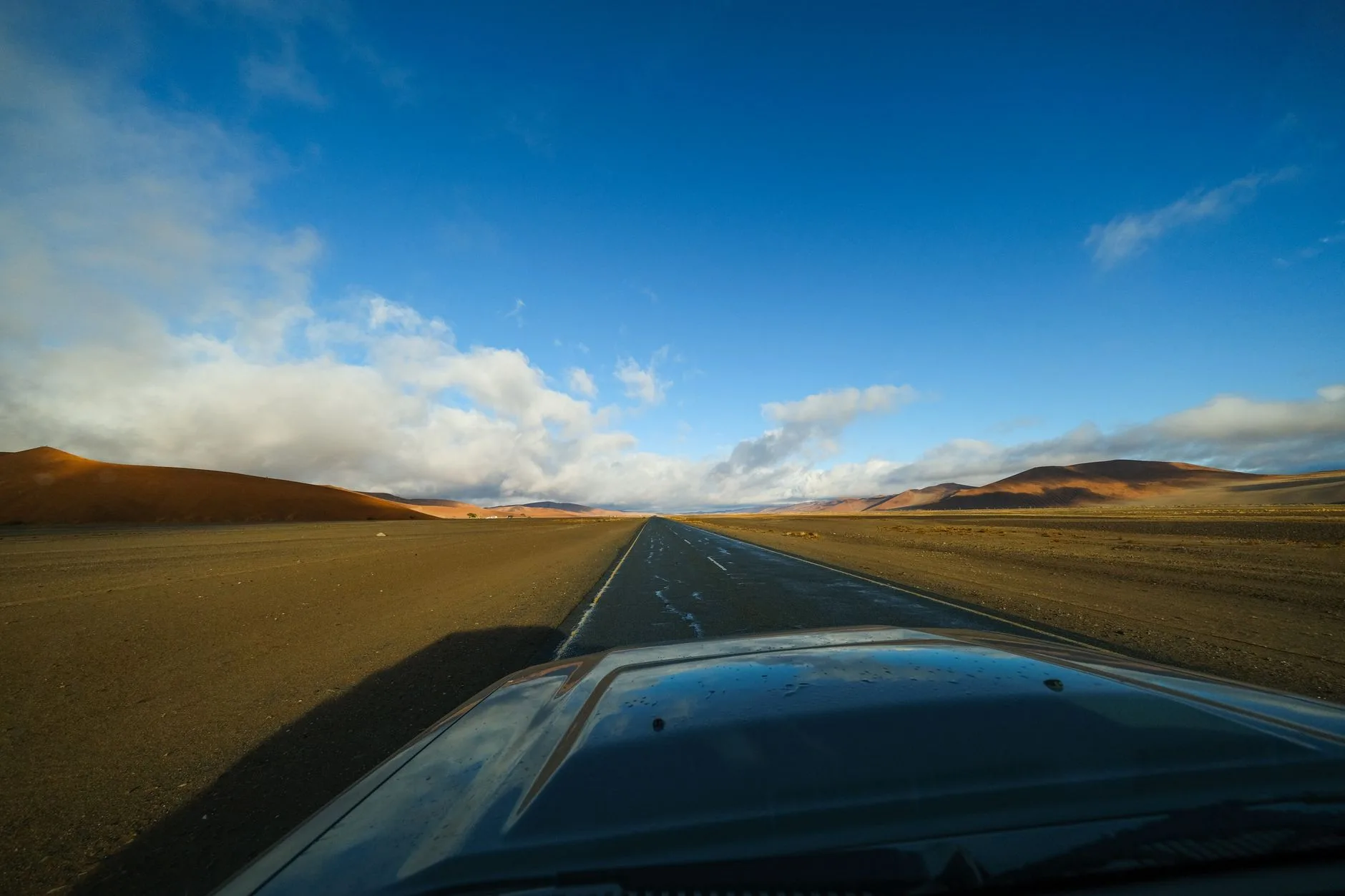 Dirt road stretching through Namibia's desert landscape under a vast blue sky